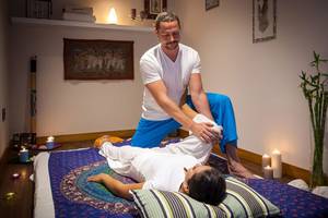 Mann führt Massage an einer Frau in einem Hotelzimmer durch, beide tragen weiße Kleidung.