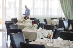 Gedeckter Tisch im Speisesaal des Eurovillage Achilleas Hotels mit Kellner im Hintergrund.