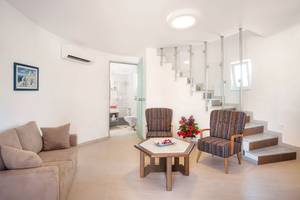 Wohnzimmer des Eurovillage Achilleas Hotels mit Couch, Stühlen und Tisch neben einer Treppe.