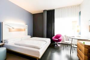 Innenansicht eines modernen Hotelzimmers im Ku Damm 101 mit zwei Betten, einem Schreibtisch und Stühlen.