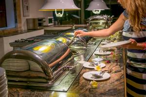 Frau bedient sich am Buffet im Le Peninsula Bay Beach Resort & Spa.