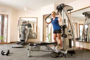 Eine Frau im blauen Shirt und schwarzen Shorts trainiert im Fitnessraum des Pinewood Beach Resort & Spa.