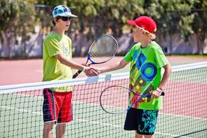 Zwei junge Spieler auf einem Tennisplatz schütteln sich die Hände.