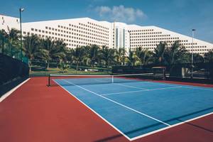 Tennisplatz vor dem Iberostar Selection Cancun Hotel mit großen Gebäuden und Palmen im Hintergrund.