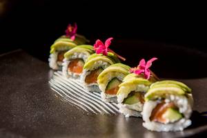 Foto von mehreren Sushi-Rollen mit Avocado und Lachs auf einem schwarzen Teller.