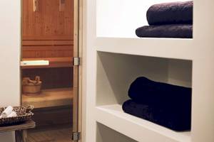 Saunabereich im Santo Pure Oia Suites & Villas mit Holzsauna, Holzkorb, Handtüchern und Holztisch.