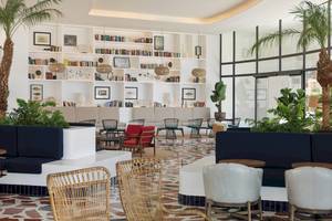 Innenansicht der Lobby des H10 Atlantic Sunset Hotels mit weißen Wänden, Bücherregalen, Pflanzen und verschiedenen Sitzgelegenheiten.
