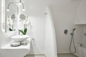Badezimmer im Katikies Chromata Hotel auf Santorini mit einem weißen Waschbecken, Spiegel und Dusche.