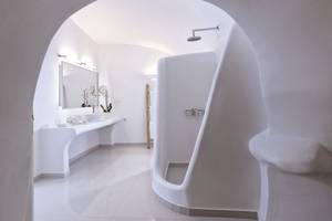 Badezimmer im Katikies Chromata Santorini Hotel mit weißer Architektur, Waschbecken und Dusche.
