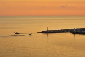 Sonnenuntergang am Wasser mit zwei Booten und einem Leuchtturm am Grecian Bay Hotel