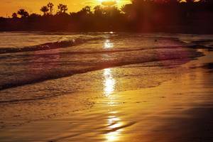 Sonnenuntergang am Strand vor dem Grecian Bay Hotel mit goldenem Licht auf dem Wasser und Palmen im Hintergrund.