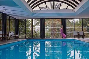 Eine Frau in einem lila Kleid steht am Rand eines blauen Swimmingpools im Grecian Bay Hotel.