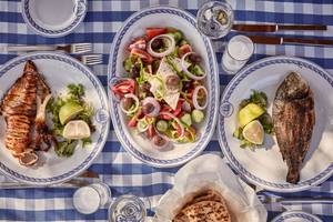Griechisches Essen auf blauem Karotisch, inklusive gegrillter Tintenfisch, Salat und gebackener Fisch.