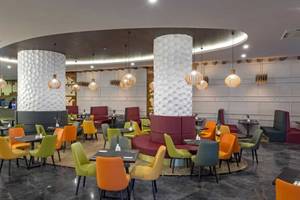 Innenansicht des Restaurants im Royal Seginus Hotel mit bunten Stühlen und Tischen, hohen Säulen und dekorativen Lampen.