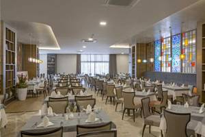Das elegante Restaurant des Royal Seginus Hotels mit vielen Tischen und Stühlen, bunten Glasfenstern und Holzregalen.