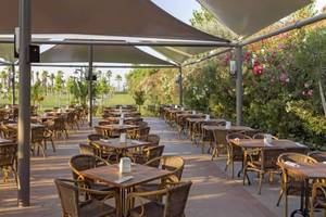 Terrasse des Royal Seginus Hotels mit vielen runden Tischen und Stühlen unter Sonnensegeln.