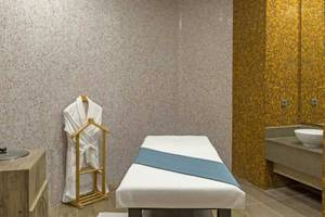 Massageraum im Royal Seginus Hotel mit einem Behandlungstisch, einem Bademantel und einem Waschbecken.