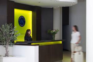 Empfang des Kriti Beach Hotels mit Rezeptionistin und Gast, die mit Gepäck unterwegs ist.