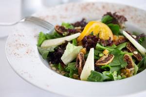 Salat in einem weißen Teller mit Obst und Nüssen.