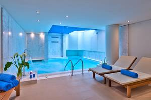 Innenpool-Bereich im Kriti Beach Hotel mit Lounge-Liegestühlen und blauen Handtüchern.
