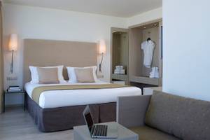 Schlafzimmer im Kriti Beach Hotel mit Doppelbett, Nachttischen und Laptop auf Beistelltisch.