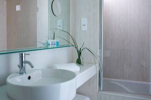 Kriti Beach Hotel Badezimmer mit einer weißen Wanne, einem Waschbecken und einem Spiegel.