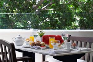 Frühstückstisch mit Obst und Getränken auf einer Terrasse mit Blick auf Bäume.