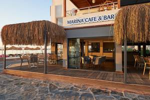 Außenansicht des Marina Cafe & Bar des Altin Yunus Hotels mit Strohdächern und Tischen im Freien.