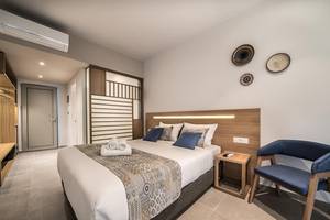 Innenansicht eines Zimmers im Adele Beach Hotel mit Doppelbett, Nachttisch und blauem Stuhl.