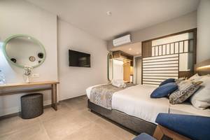 Innenansicht eines Zimmers im Adele Beach Hotel mit Bett, Nachttisch und Spiegel.