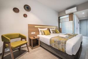 Ein elegantes Hotelzimmer im Adele Beach Hotel mit einem Bett, gelben Kissen und einem grünen Stuhl.