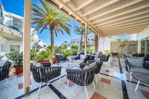 Terrasse des Adele Beach Hotels mit Lounge-Sesseln und Pflanzen, beschattet von einer Pergola.