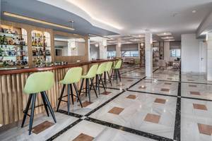 Innenansicht der Bar im Adele Beach Hotel mit grünen Stühlen und einer Theke voller Alkoholflaschen.