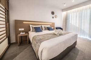 Schlafzimmer im Adele Beach Hotel mit großem Bett, Kissen und Decken, neben einem Nachttisch
