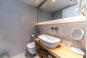 Badezimmer im Adele Beach Hotel mit grauen Fliesen, Toilette, Waschbecken und Spiegeln.