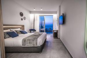 Innenansicht eines Hotelzimmers im Adele Beach Hotel mit einem Doppelbett, einem Fernseher und einem Balkon.