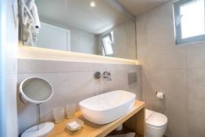 Badezimmer im Adele Beach Hotel mit Waschbecken, Spiegel, Toilette und Fenster.