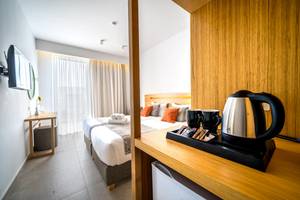 Innenansicht eines Hotelzimmers im Adele Beach mit zwei Betten, Fernseher, Tisch und Kaffeemaschine.