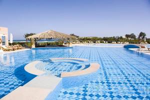 Poolbereich des Mövenpick Resort & Spa El Gouna mit Loungeliegen und einer Palmhütte.