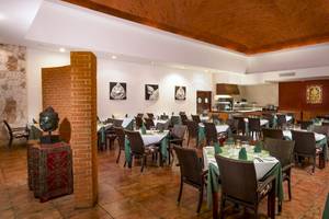Innenansicht des Restaurants im Grand Sirenis Riviera Maya Resort & Spa mit gepolsterten Stühlen und gedeckten Tischen.