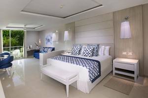 Ein elegantes Schlafzimmer im Grand Sirenis Riviera Maya Resort & Spa mit einem großen Bett, blauen Kissen und einer modernen Einrichtung.