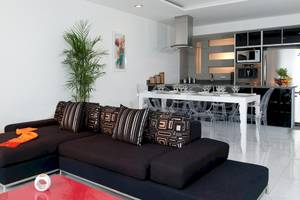 Modernes Wohnzimmer des Grand Sirenis Riviera Maya Resort mit schwarzem Sofa, weißem Esstisch und stilvoller Küche im Hintergrund.