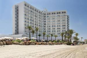 Außenansicht des Roc Barlovento Hotels am Strand mit vielen Palmen und einem blauen Himmel.