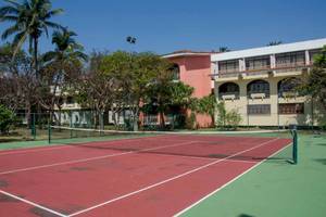 Tennisplatz vor dem Roc Barlovento Hotel mit roten und grünen Spielflächen und Bäumen im Hintergrund.