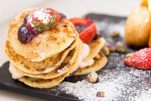 Stapel goldener Pfannkuchen mit Beeren und Sahne auf einem schwarzen Teller