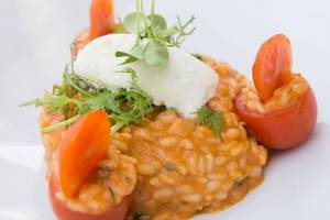 Ein Gericht mit Risotto, Tomaten und Frischkäse auf einem weißen Teller.
