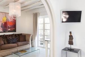 Wohnzimmer im Kivotos Mykonos Hotel mit Couch, Glastisch, Gemälde, Fernseher und Dekor.