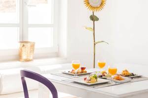 Frühstückstisch im Kivotos Mykonos Hotel mit Orangensaft, Speisen und einer Sonnenblume im Hintergrund.