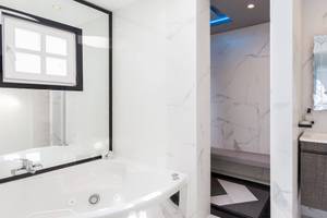 Das Badezimmer von Kivotos Mykonos mit einer Badewanne, einer Dusche, einem Spiegel und einem Waschbecken.