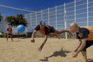 Zwei Männer spielen Volleyball am Strand mit einem blauen Ball.